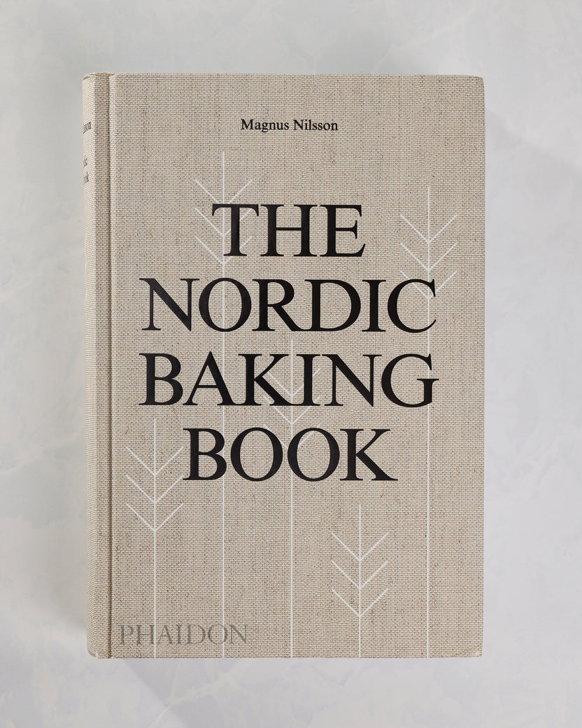 Front cover of The Nordic Baking Book by Magnus Nilsson, featuring large black title lettering and white stylized tree outlines on a light background.