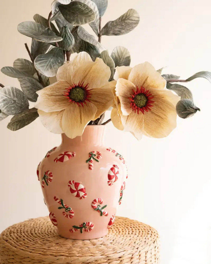 Pink ceramic vase with peppermint decorations holding a dried floral arrangement on a woven stand