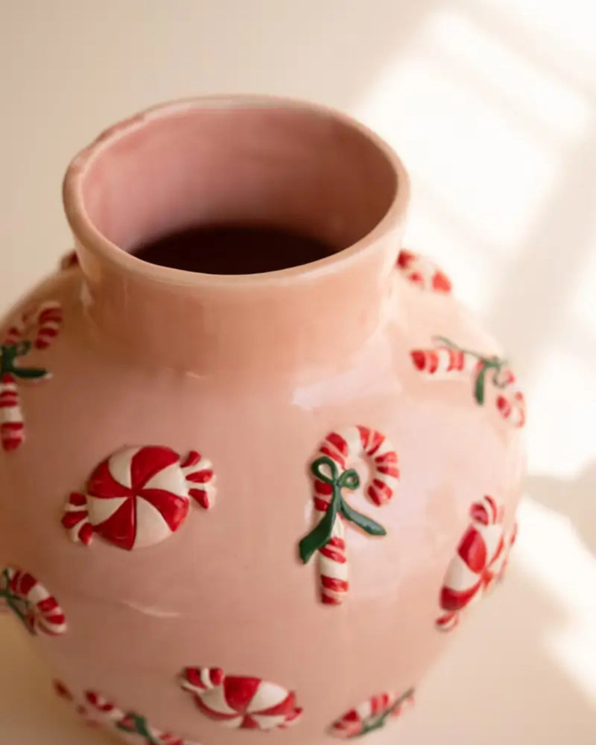 Close-up of a glossy pink ceramic vase decorated with raised red-and-white peppermint candies and candy canes.