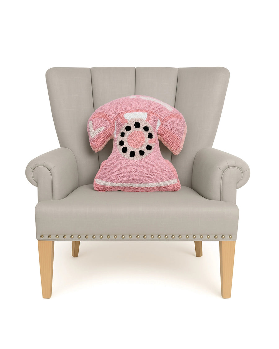 Pink telephone-shaped hook pillow displayed on a light upholstered armchair