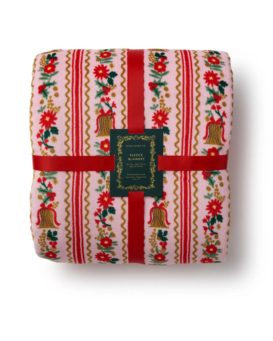 Ribbon-wrapped fleece blanket in a pink floral-and-bell print, packaged with a red ribbon and a central product label.