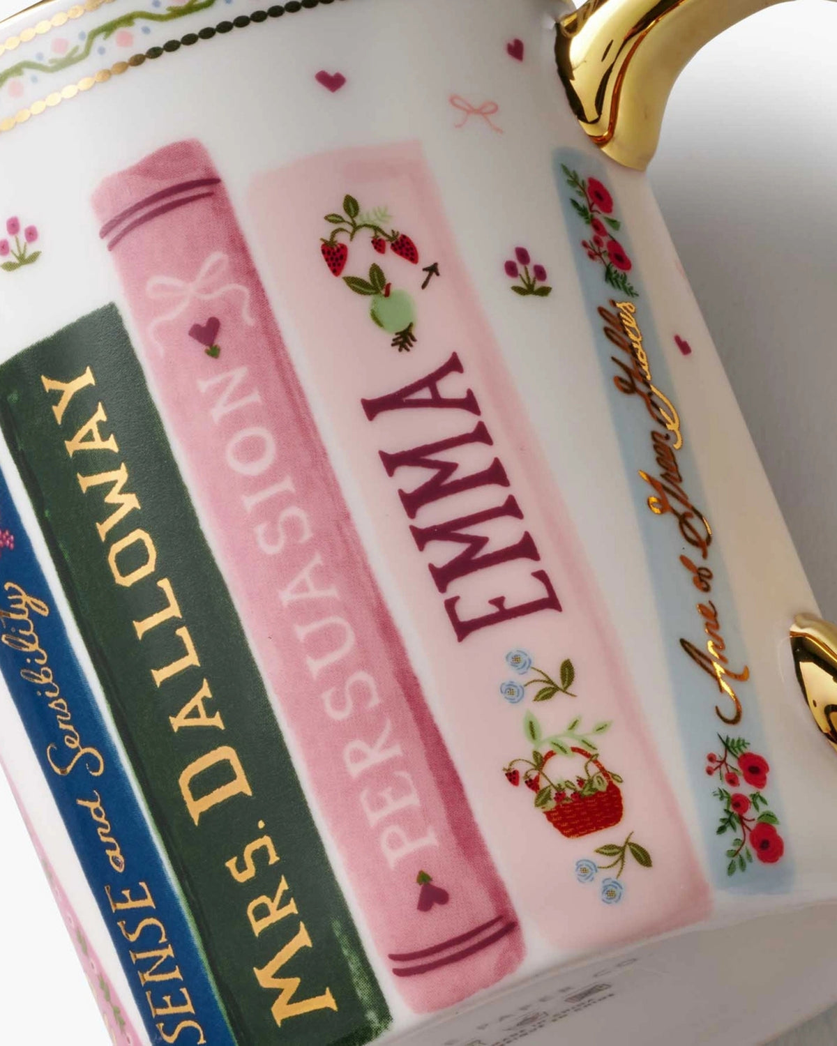 Close-up of a mug decorated with an illustrated stack of floral books and a gilded handle.