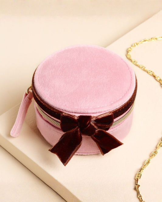 Closed pink round travel jewelry case with a brown bow and gold zipper.