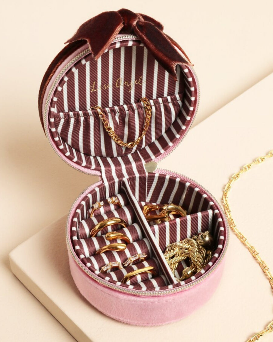 Open pink round jewelry case showing striped lining, ring rolls, compartments, and jewelry storage.