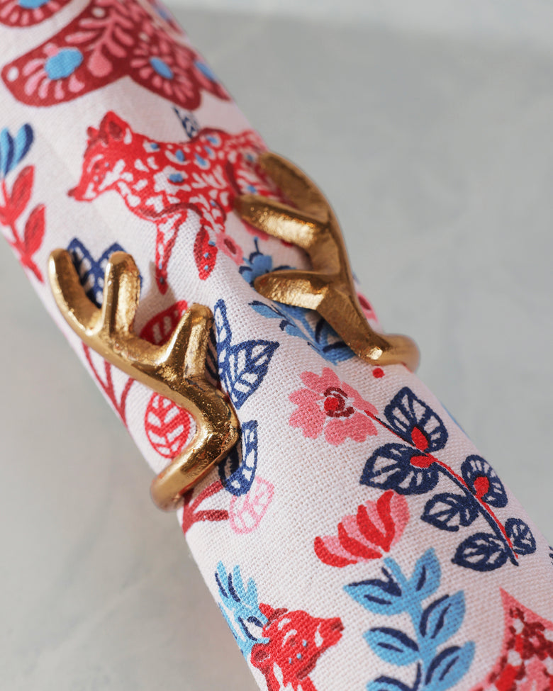 Close-up of a gold antlers napkin ring around a rolled white napkin with a red, blue, and pink floral pattern.