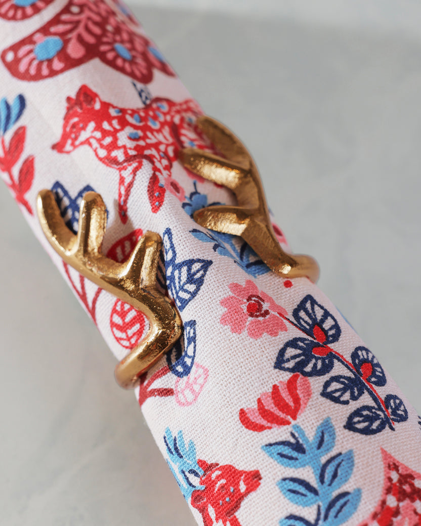 Close-up of a gold antlers napkin ring around a rolled white napkin with a red, blue, and pink floral pattern.