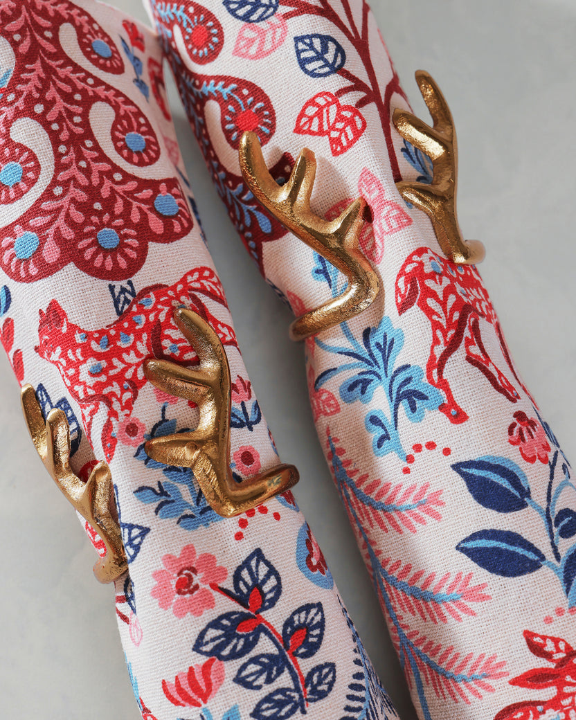 Close-up of two gold antlers napkin rings around rolled white napkins with colorful floral patterns.