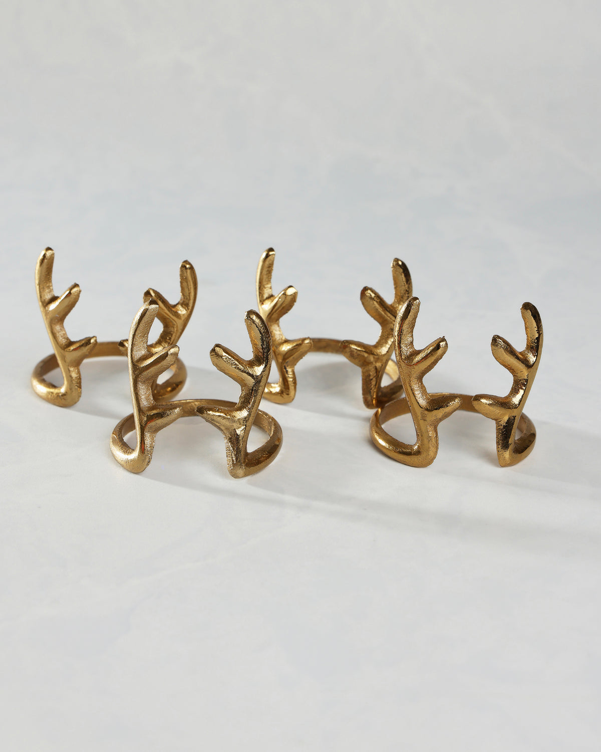 Several gold antlers napkin rings arranged in two rows on a white surface.