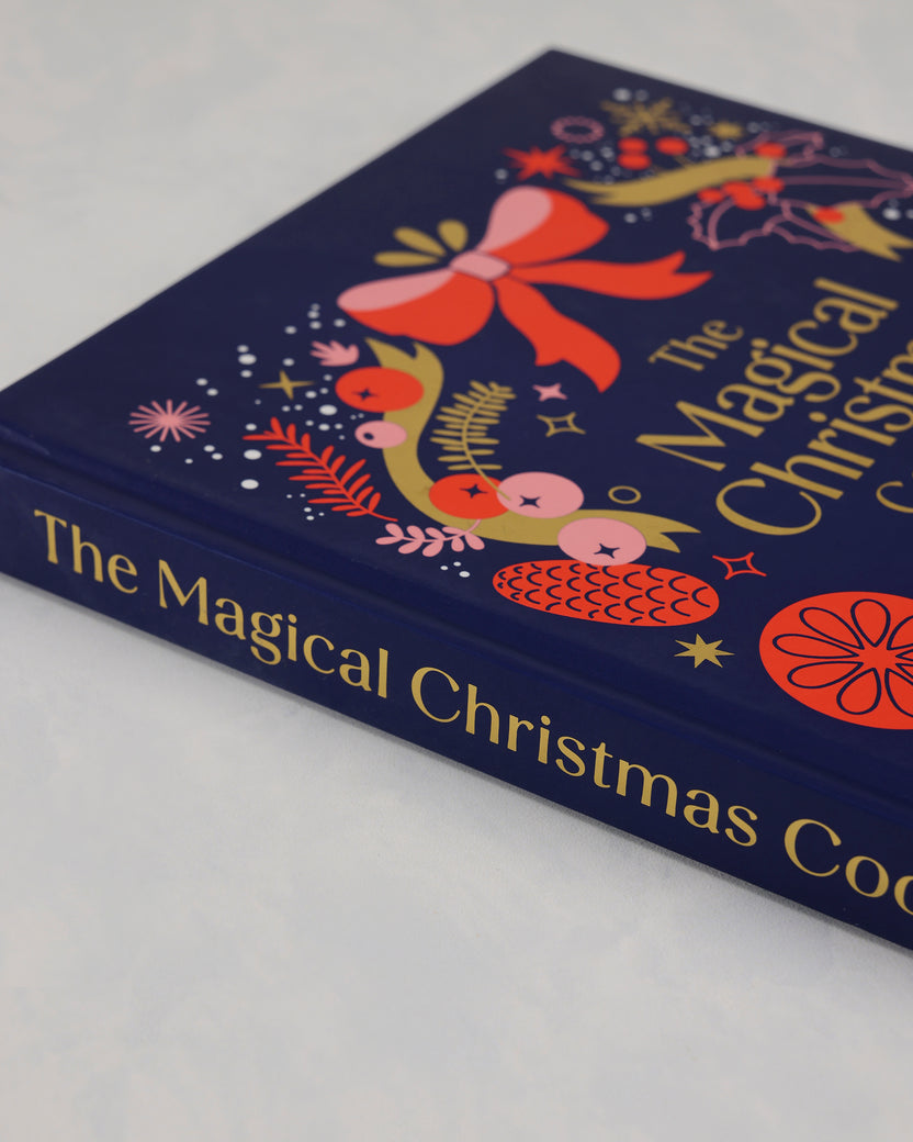 Angled close-up of the front cover and spine of The Magical Christmas Cookbook with colorful Christmas illustrations.
