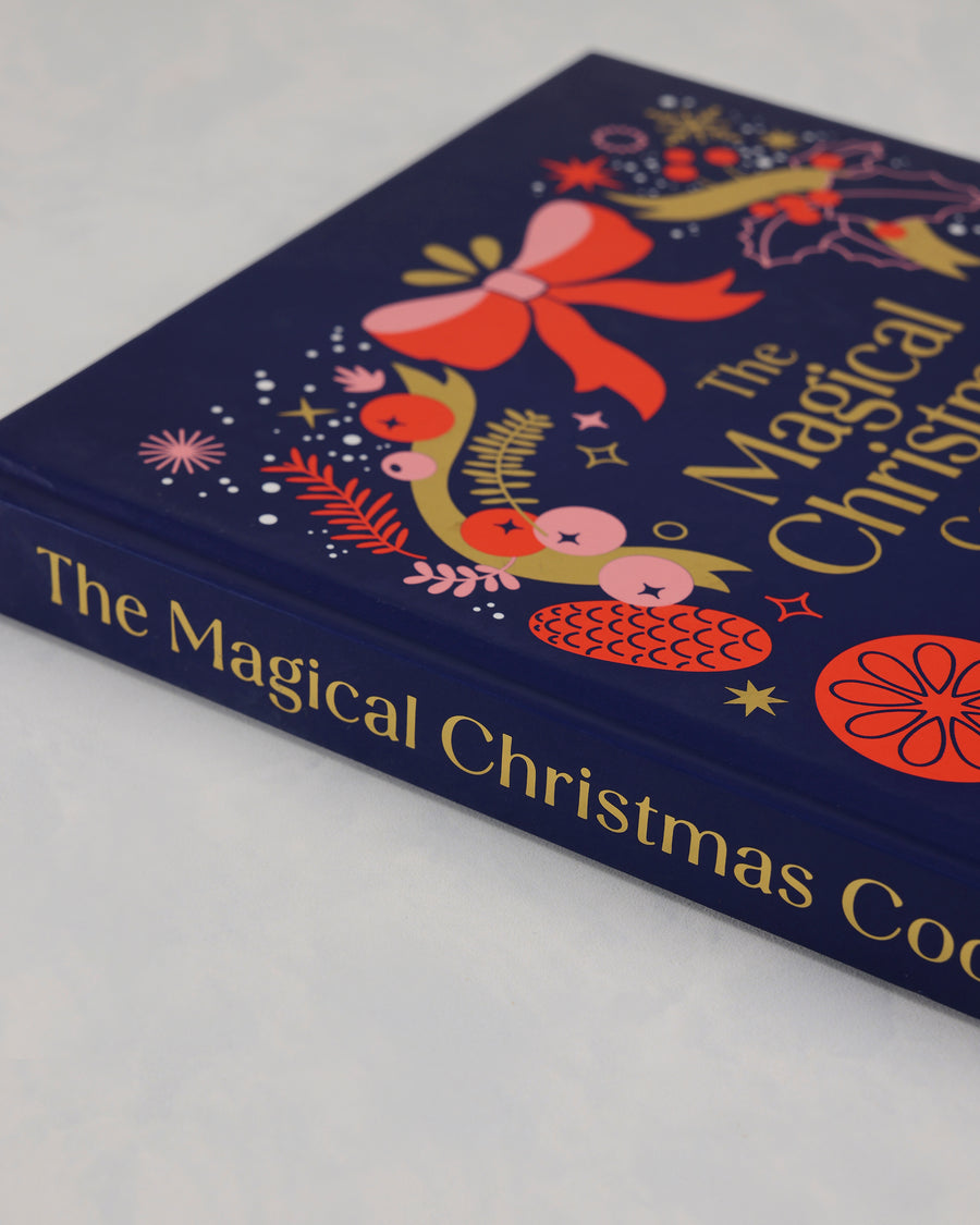 Angled close-up of the front cover and spine of The Magical Christmas Cookbook with colorful Christmas illustrations.