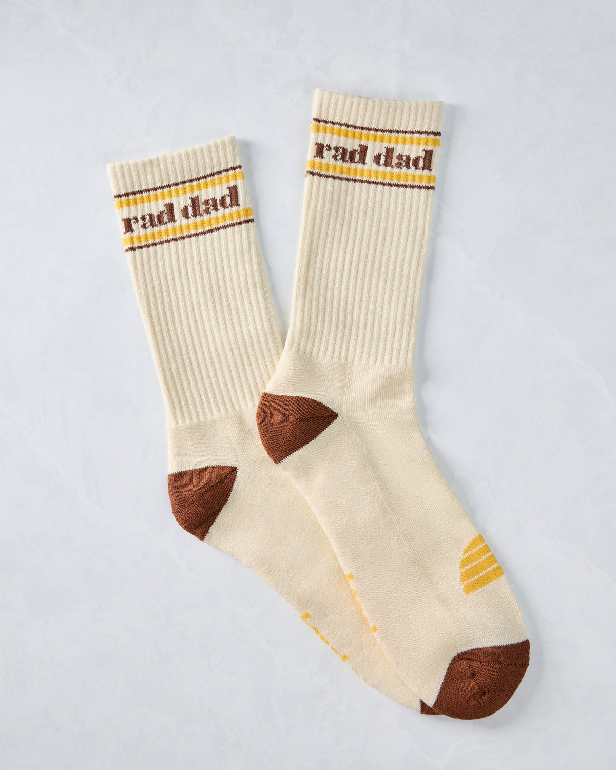 Pair of ivory crew socks with brown and yellow stripes, “Rad Dad” lettering, brown heels and toes, and yellow accents.