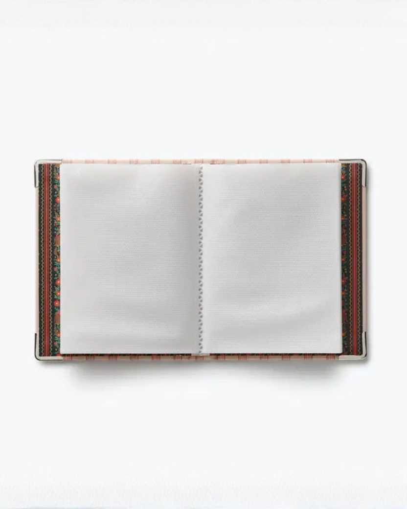Open small photo album showing blank pages, patterned inner covers, and metal corner protectors.