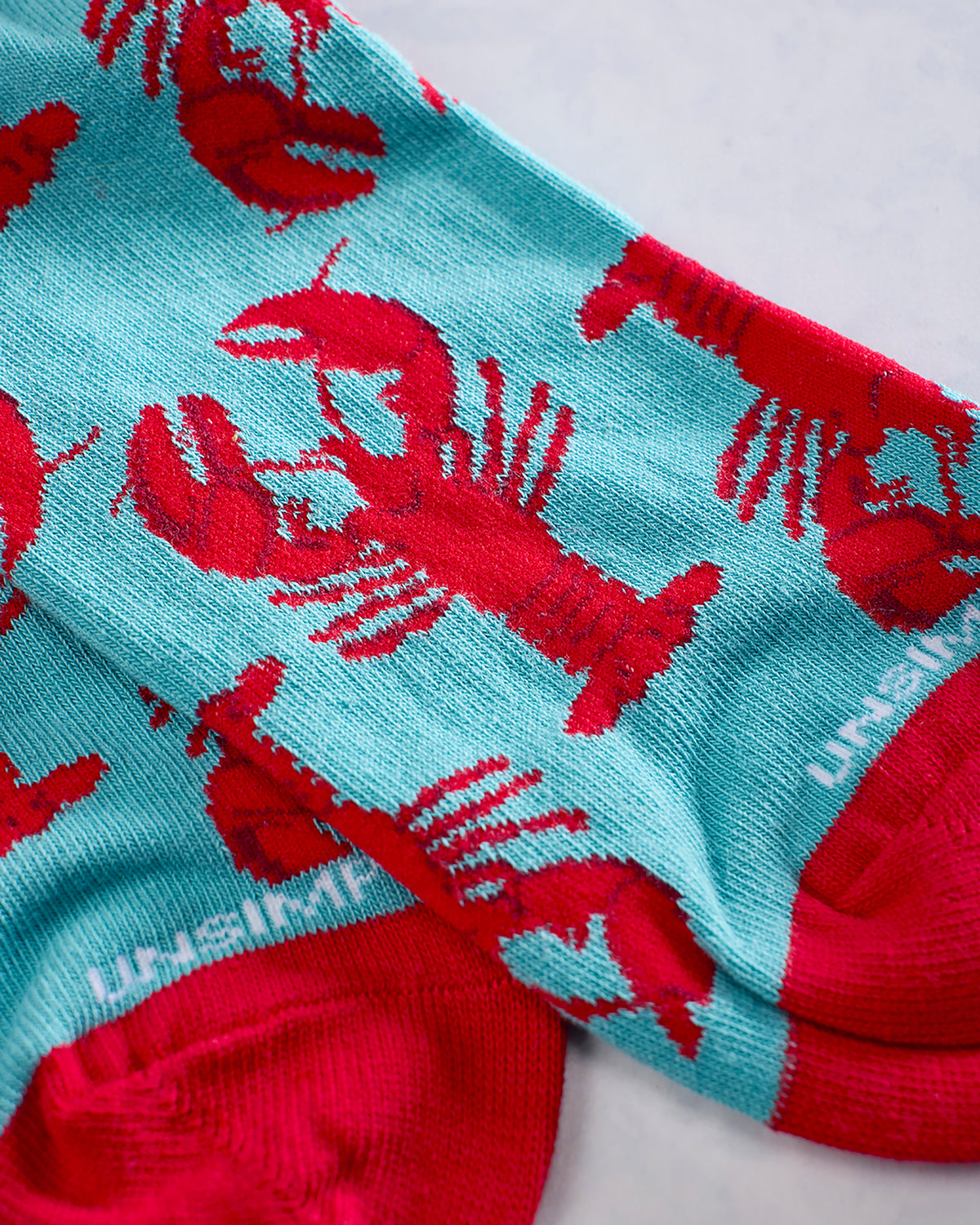 Close-up of turquoise socks with a red lobster pattern and red cuffs.