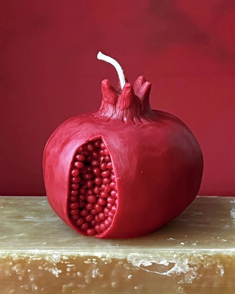 Red pomegranate-shaped beeswax candle with a white wick on a wooden surface.