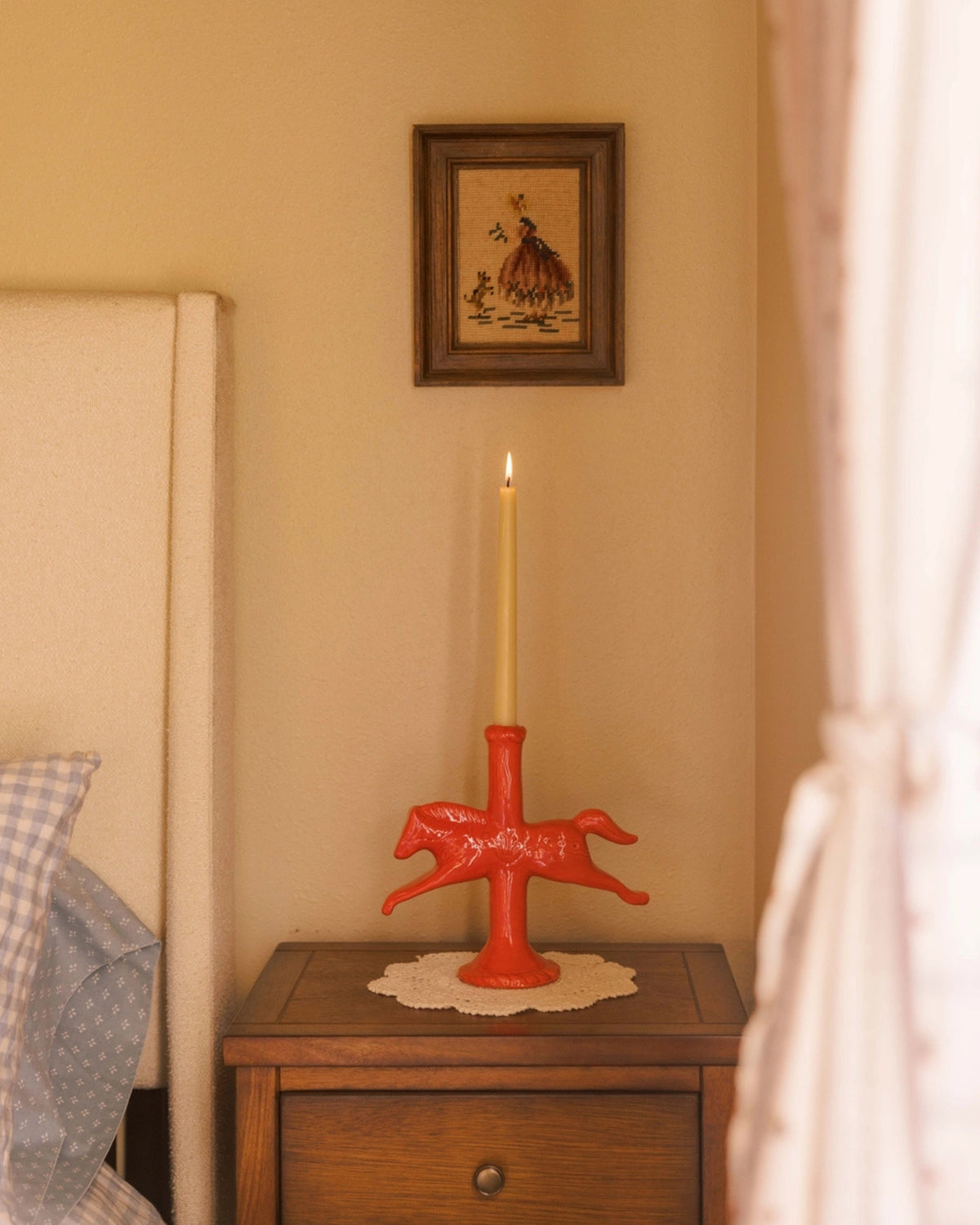 Red horse-shaped candlestick holder with a lit taper candle displayed on a bedside table.