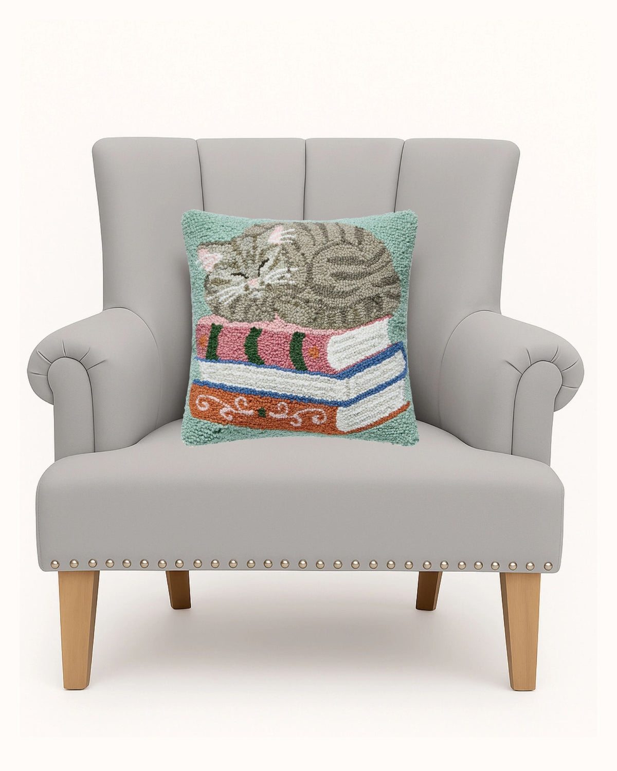 Cat-on-books pillow displayed on a gray armchair.