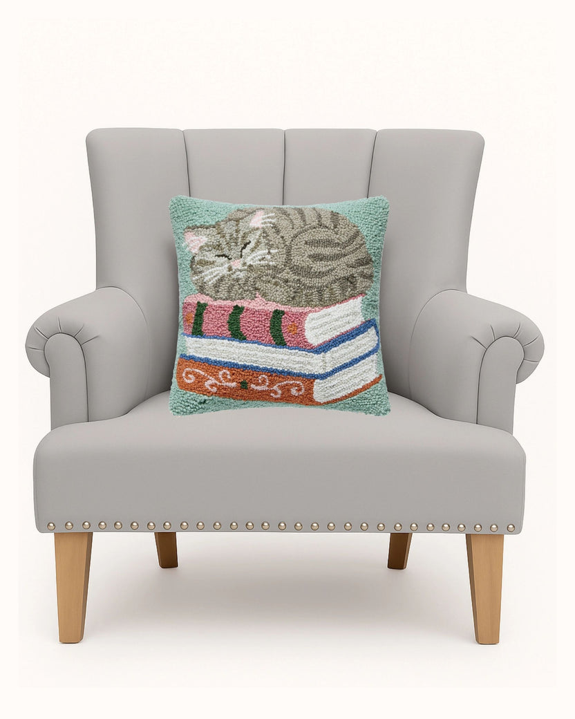Cat-on-books pillow displayed on a gray armchair.