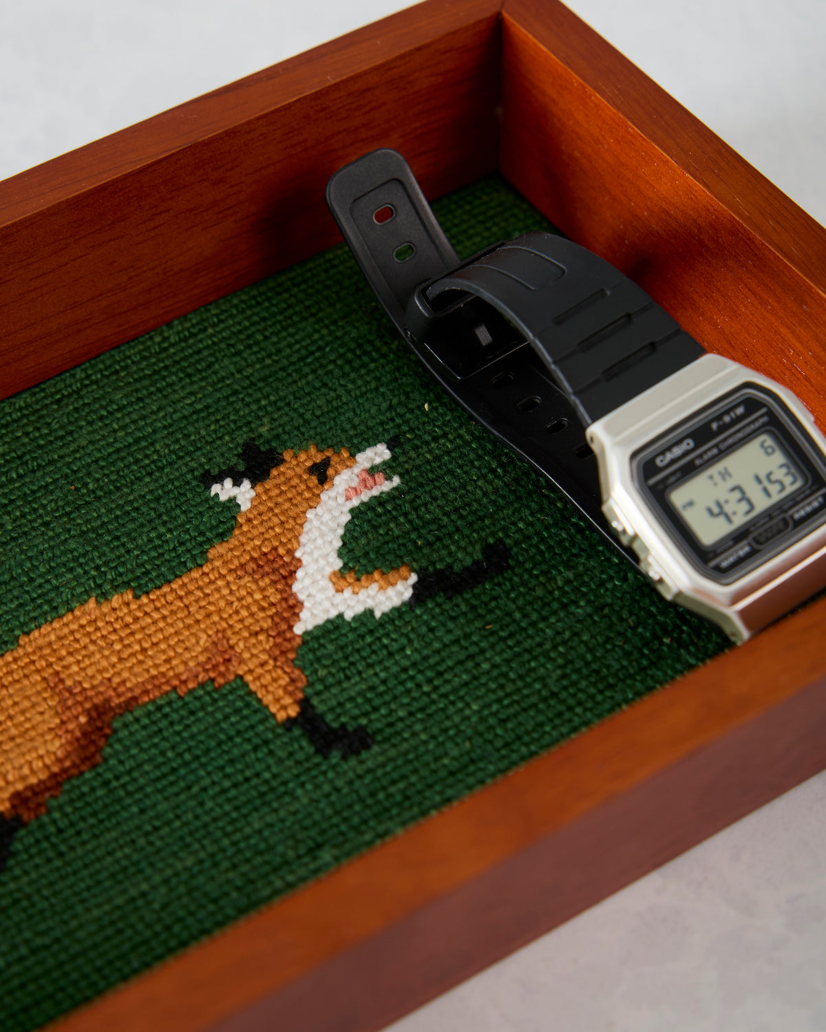 Wooden fox valet tray with a green needlepoint inlay, shown holding a digital watch.