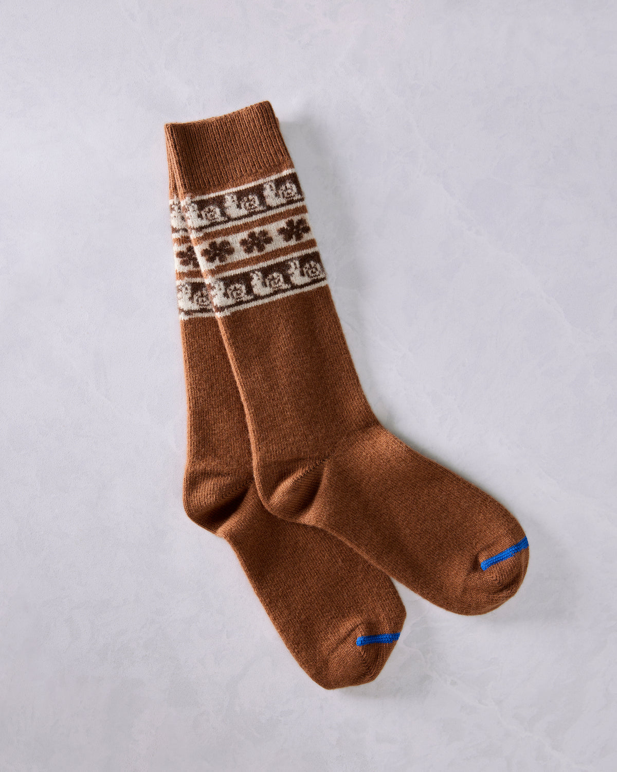 Pair of brown crew socks with cream Fair Isle bands featuring snail motifs and contrasting blue toe seams.