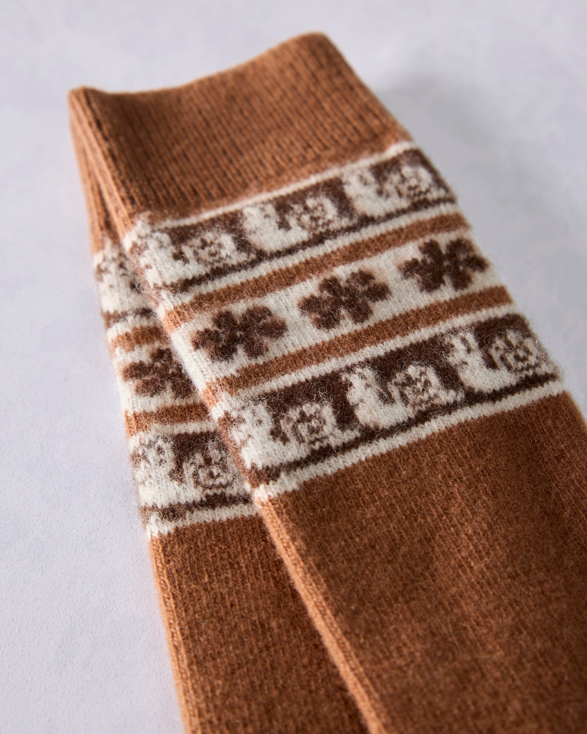 Close-up of brown crew socks showing cream Fair Isle bands with snail motifs and repeated decorative lettering.