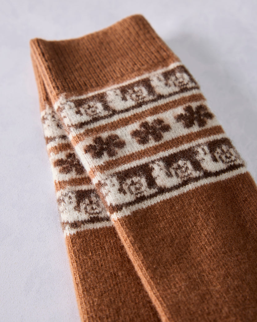 Close-up of brown crew socks showing cream Fair Isle bands with snail motifs and repeated decorative lettering.