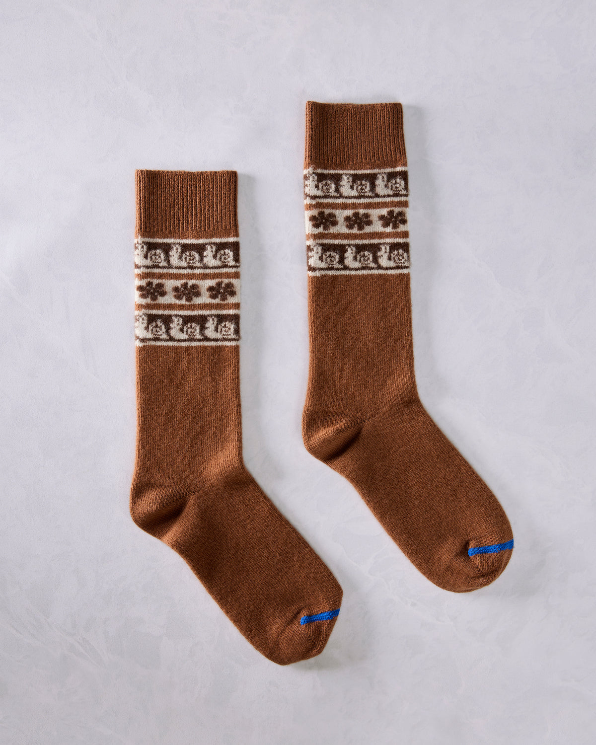 Pair of brown crew socks laid flat, with cream snail-patterned Fair Isle bands and blue toe seams.