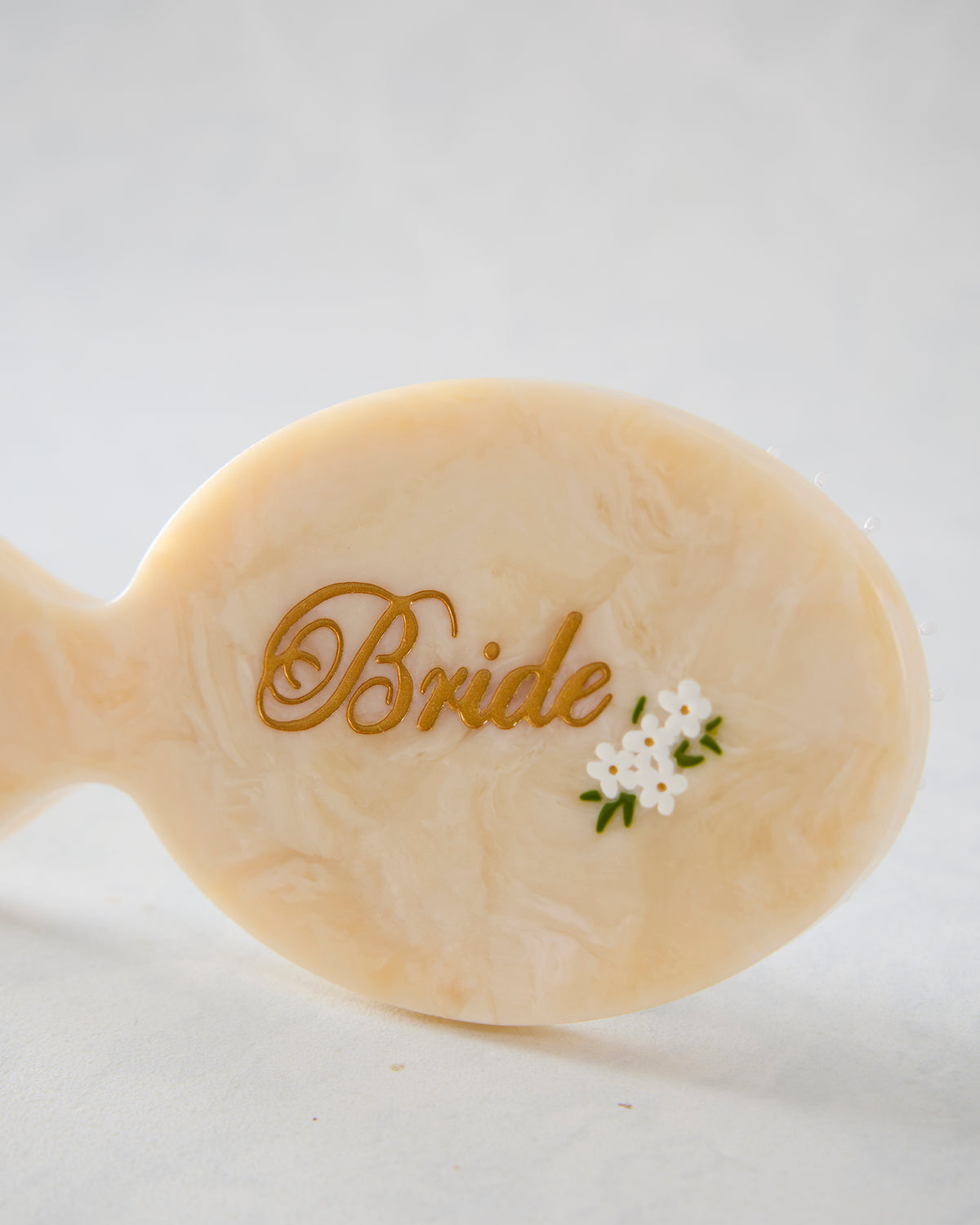 Close-up of the cream hairbrush handle showing gold “Bride” lettering and a small white flower decoration.