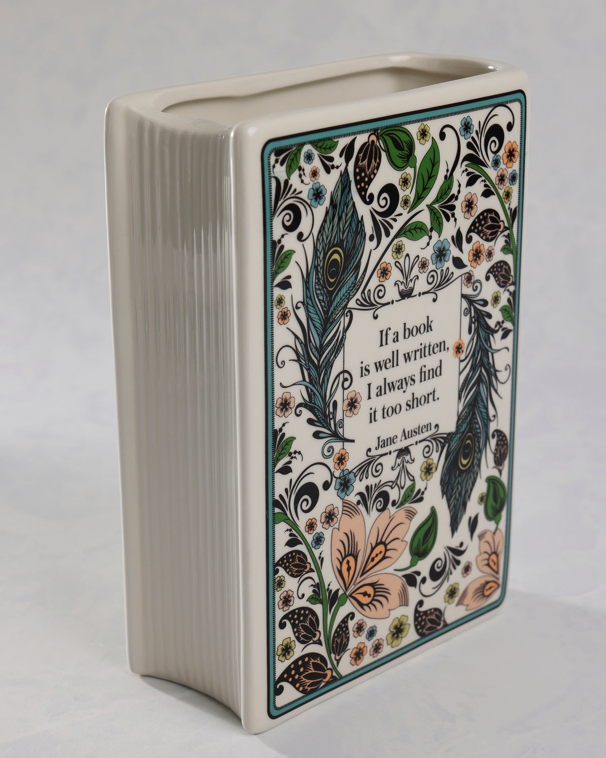 Angled view of the Jane Austen book-shaped vase showing its floral and peacock-feather side artwork and open top.