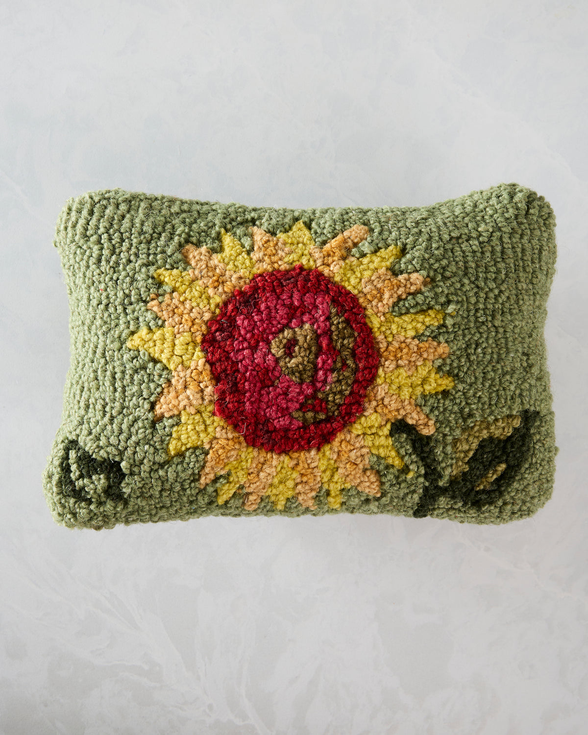 Front of a rectangular hooked pillow featuring a red and yellow sunflower on a green background.