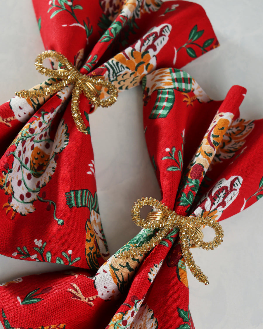 Gold bow napkin rings securing red patterned cloth napkins.