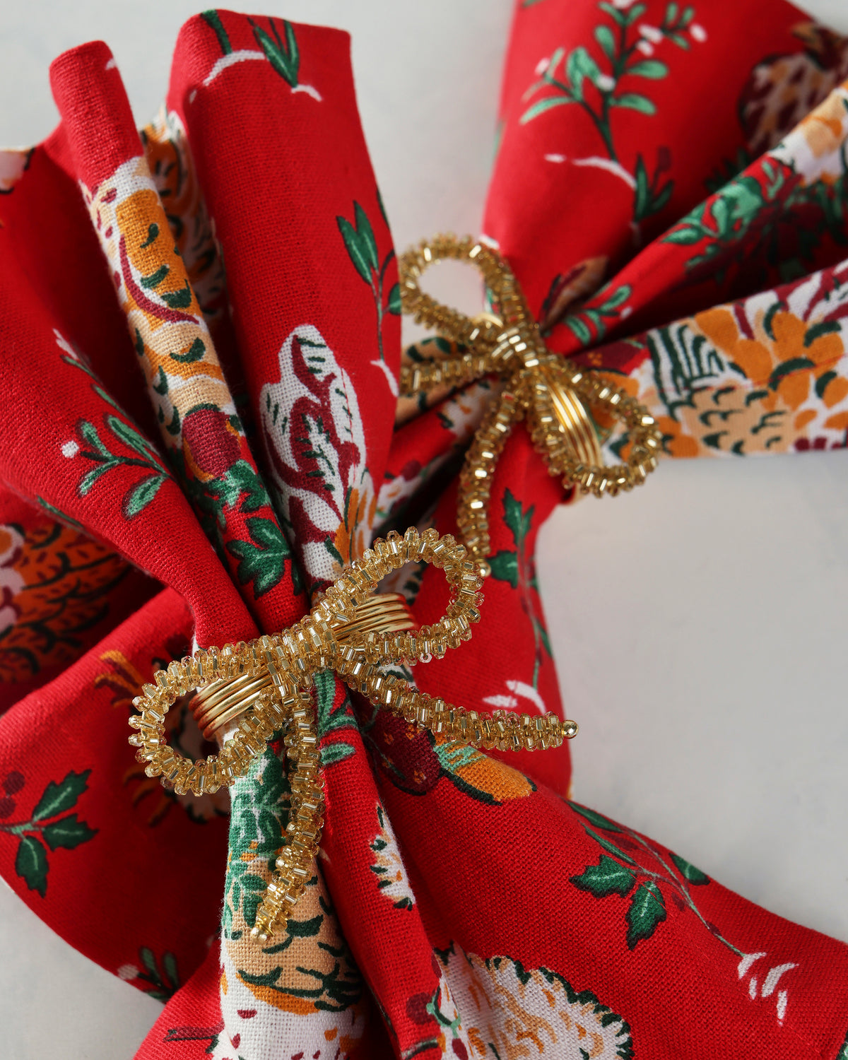 Gold bow napkin rings securing folded red patterned cloth napkins in a close-up view.