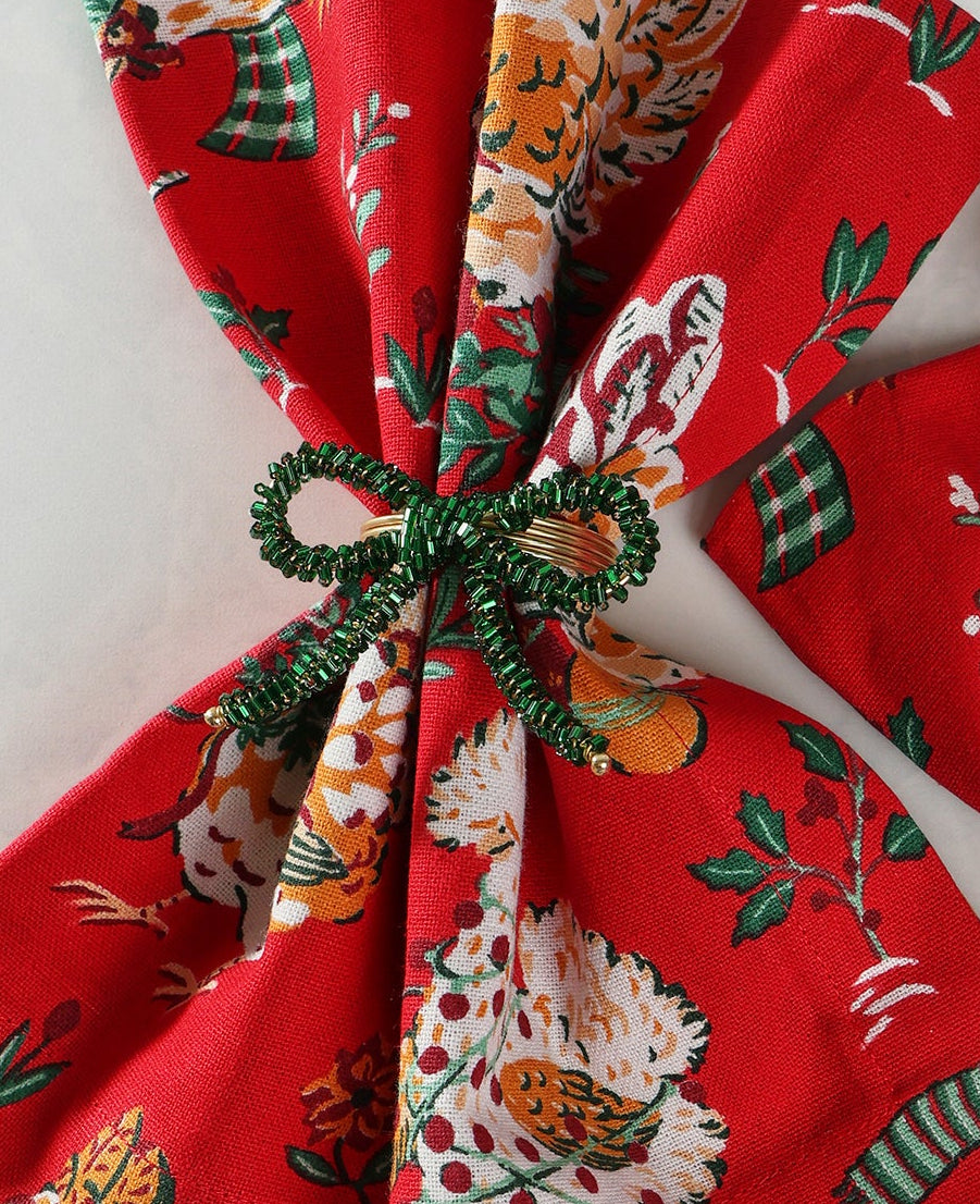 Two green bow napkin rings securing red patterned cloth napkins.