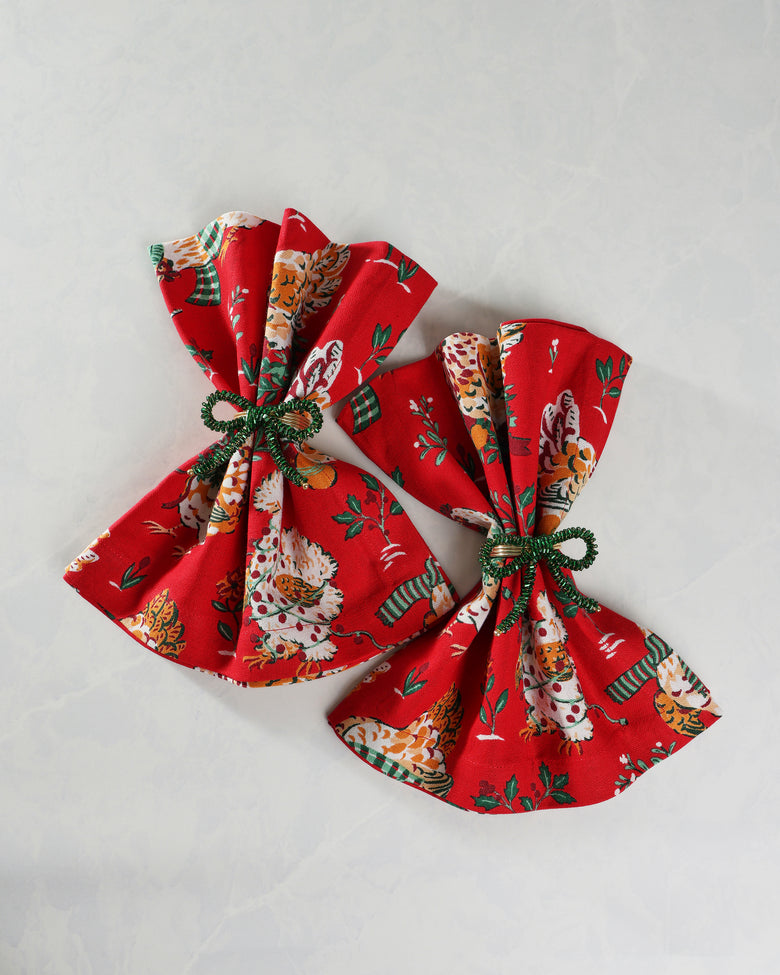 Two green bow napkin rings securing red patterned cloth napkins.