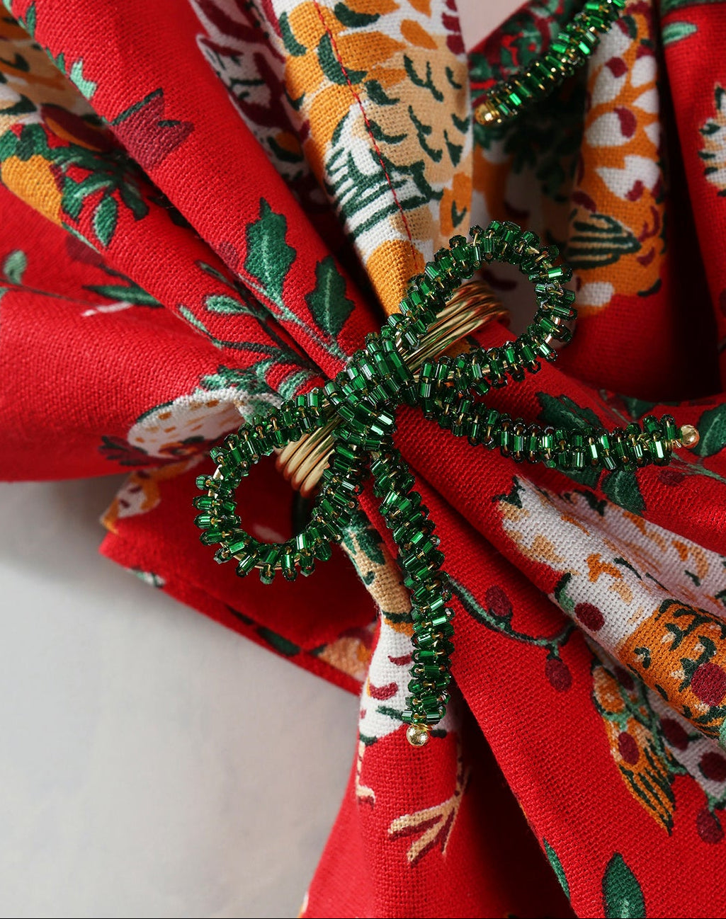 Green beaded bow napkin ring shown securing a folded patterned napkin