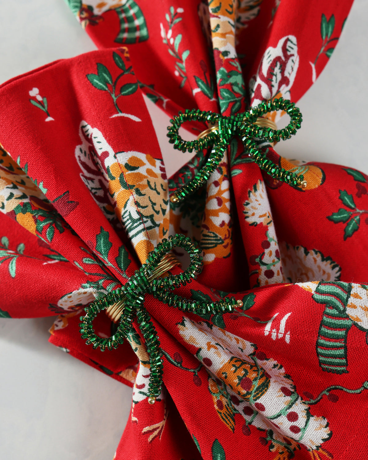 Green beaded bow napkin ring shown securing a folded patterned napkin