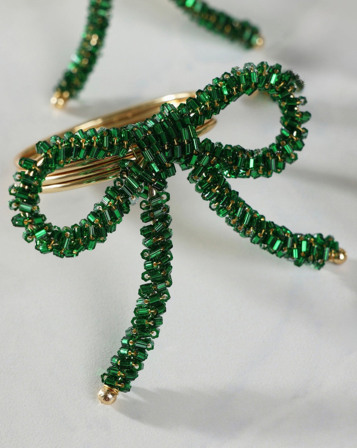 Green beaded bow napkin ring with a gold-tone metal center and dangling beaded tails