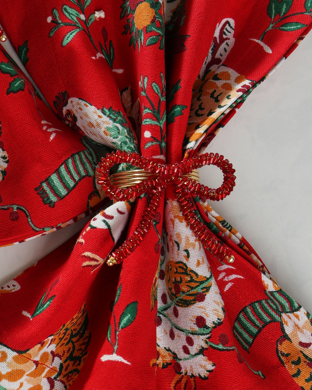 Red beaded bow napkin rings shown securing folded patterned napkins