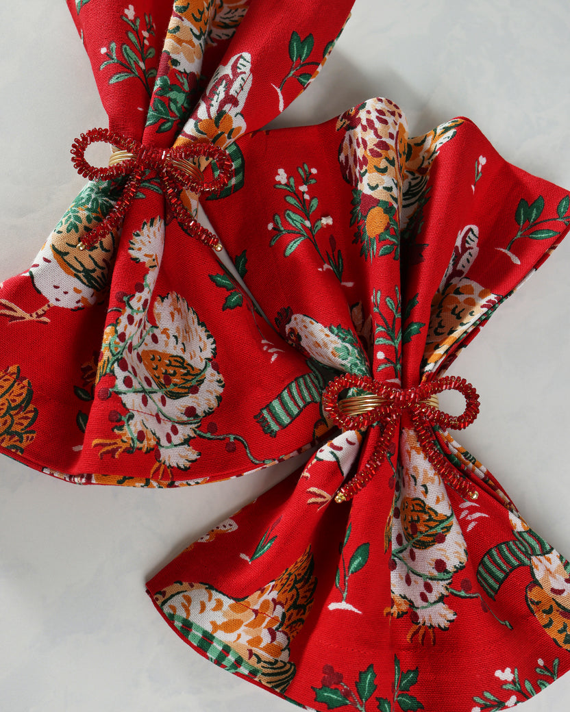 Red beaded bow napkin rings shown securing folded patterned napkins