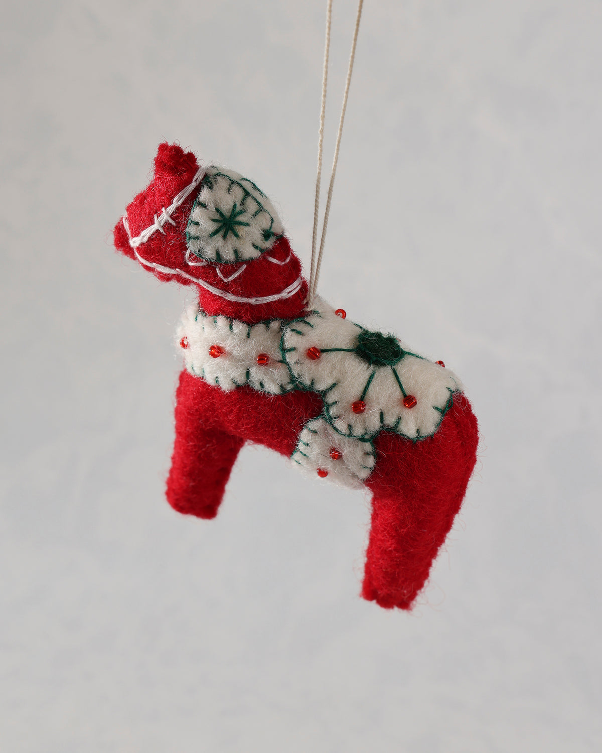 Angled view of a red and ivory dala horse ornament with a hanging loop
