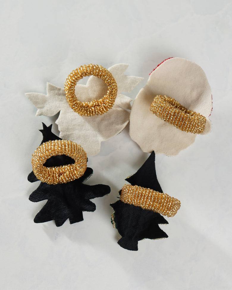 Back view of four holiday napkin rings showing gold circular bands attached to white and black decorative shapes.