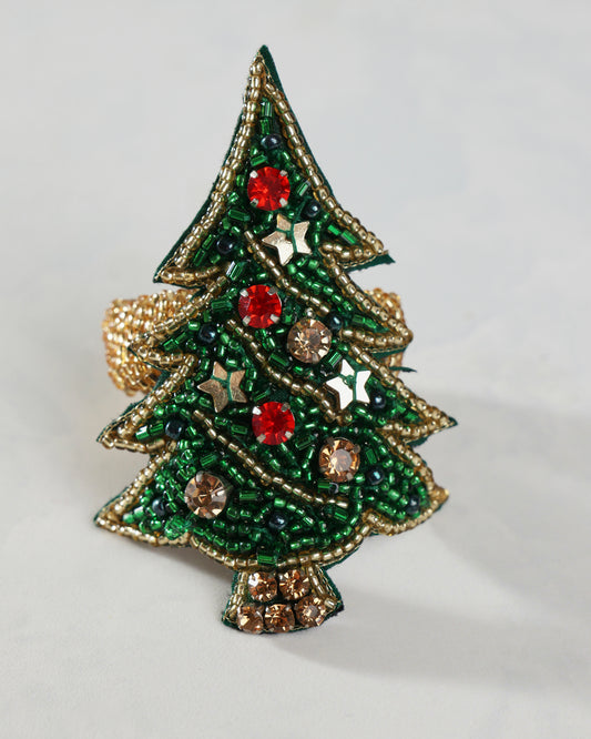 Close-up of a green Christmas tree napkin ring decorated with gold beadwork, red and gold ornaments, stars, and a jeweled trunk.