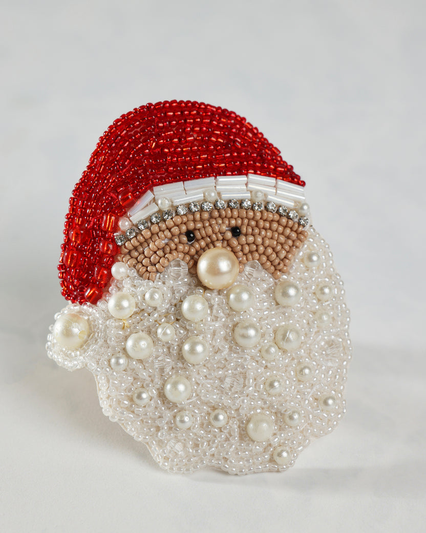 Close-up of a Santa napkin ring with a red beaded hat, tan face, white beaded beard, and pearl-like accents.