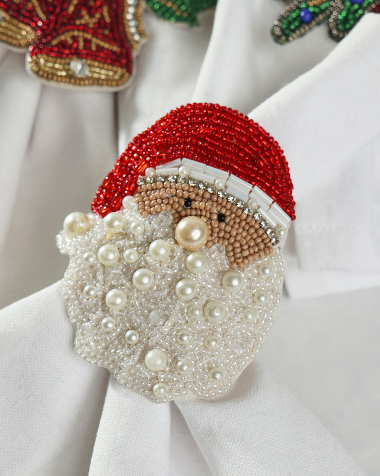 Angled close-up of a Santa napkin ring showing its red beaded hat, tan face, white beard, and pearl-like embellishments.