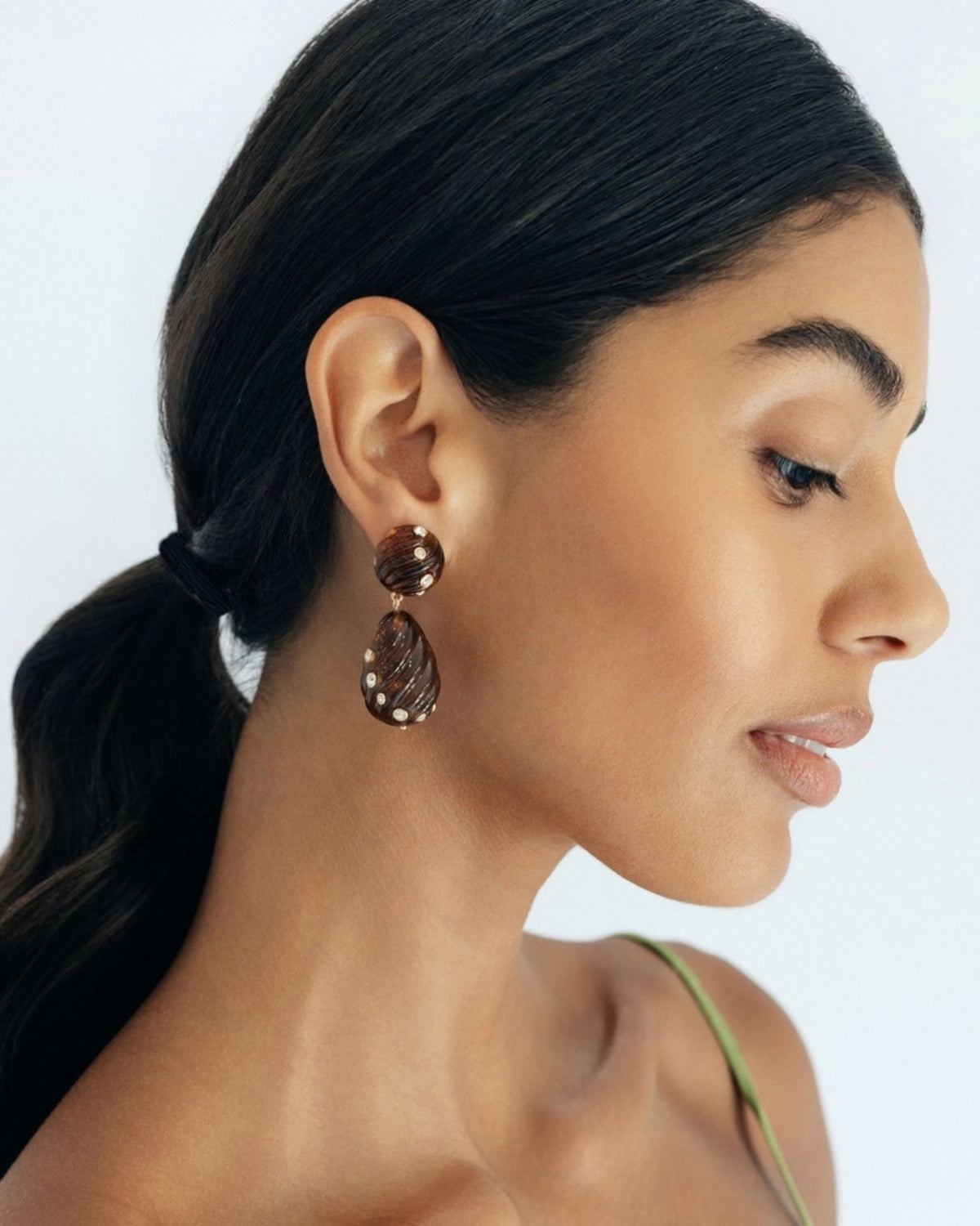 Side-profile view of a person wearing a brown ridged tortoise drop earring with small clear stones.