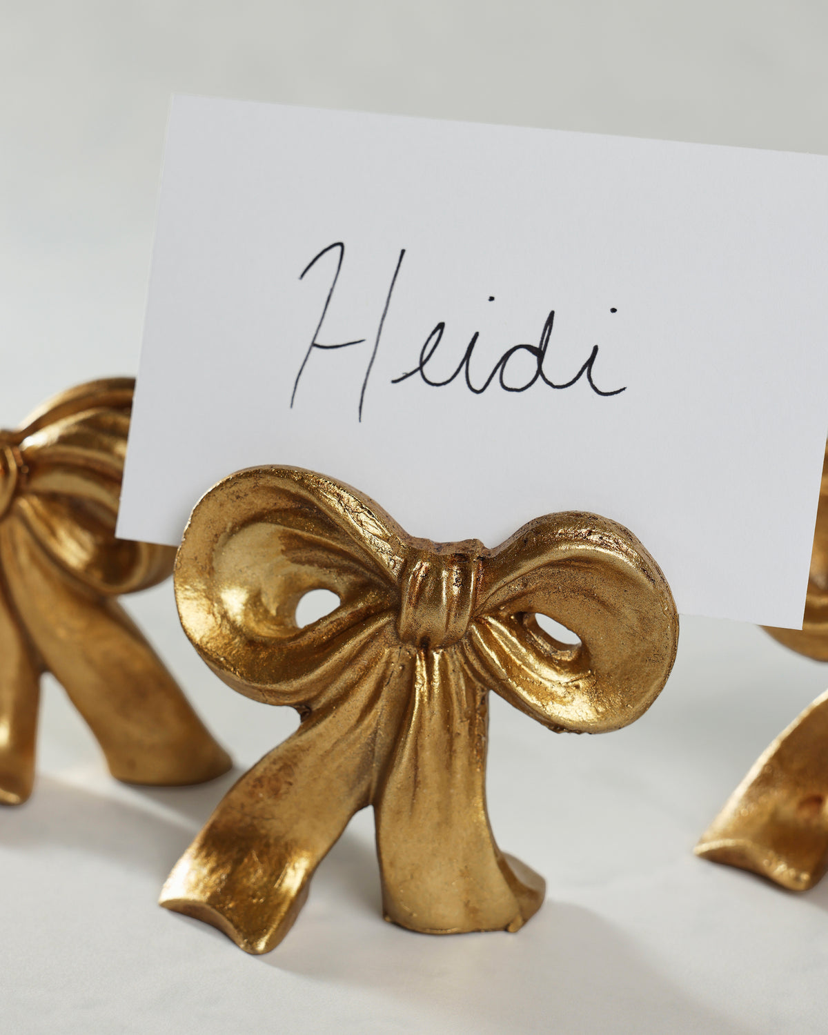 Close view of a gold bow placecard holder beneath a card labeled “Heidi.”