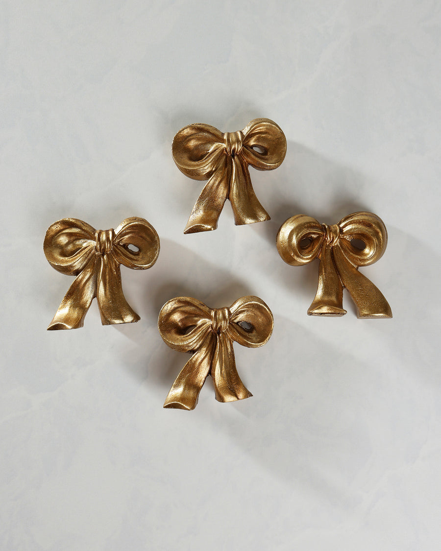 Four gold bow placecard holders arranged separately on a light background.