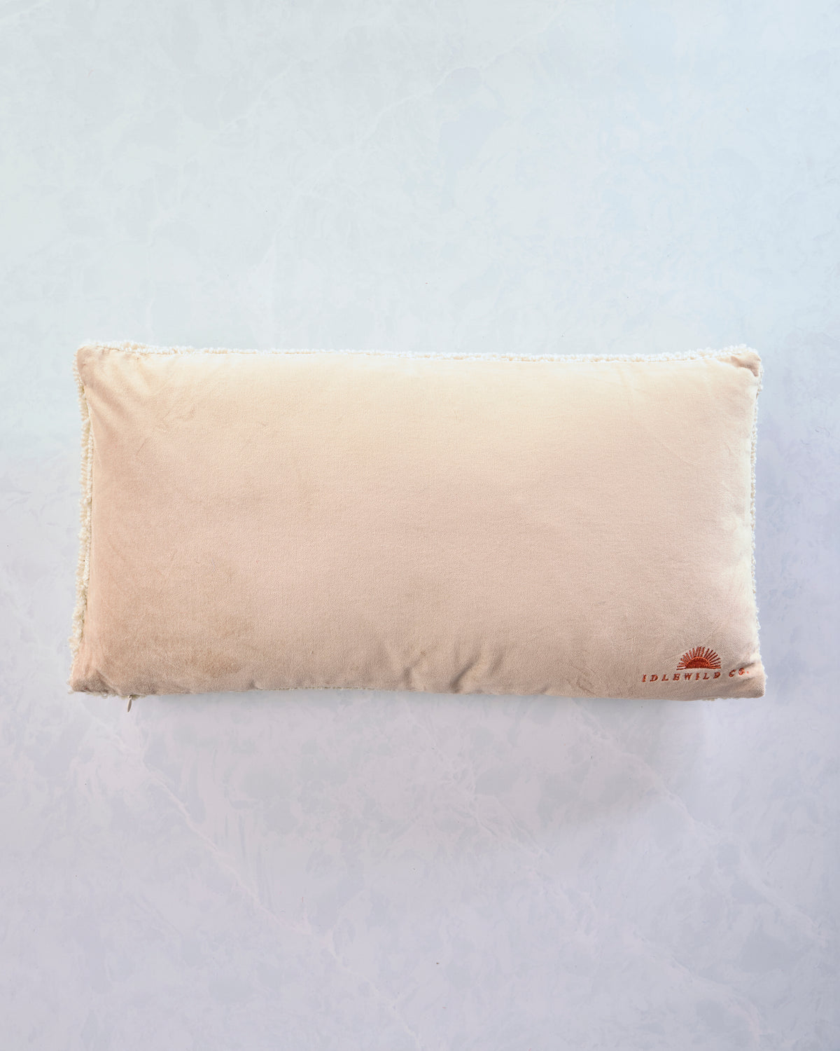 Back of a cream rectangular lumbar pillow with the Idlewild Co. logo in the lower-right corner and white edging.