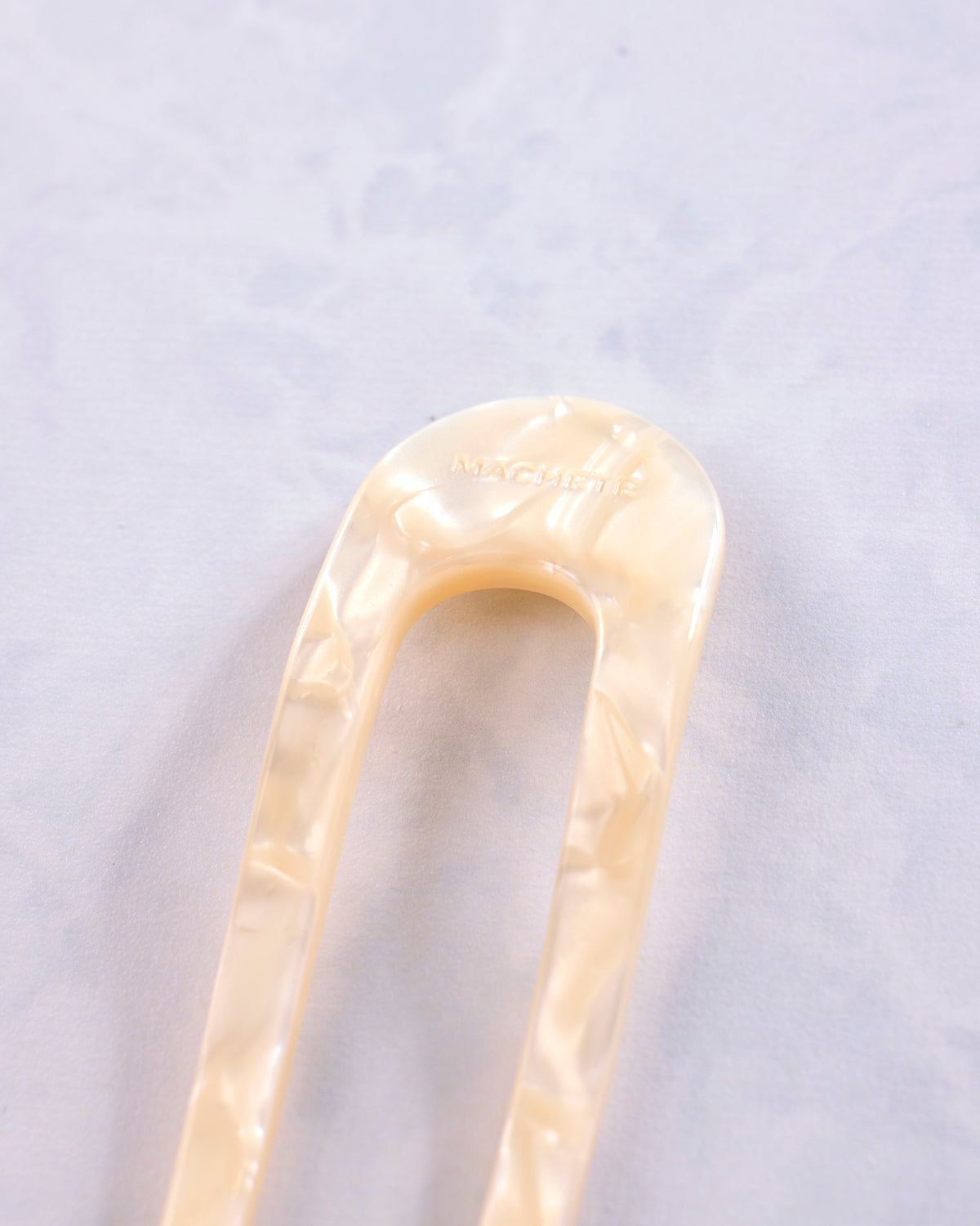 Close-up of the cream-colored rounded end of a Machete French hair pin.