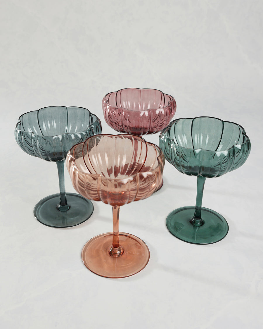 Four flower-shaped coupe glasses in pink, peach, blue, and green tones arranged together.