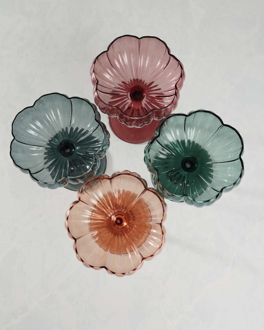 Top-down view of four scalloped flower-shaped coupe glasses in pink, blue, green, and peach tones.